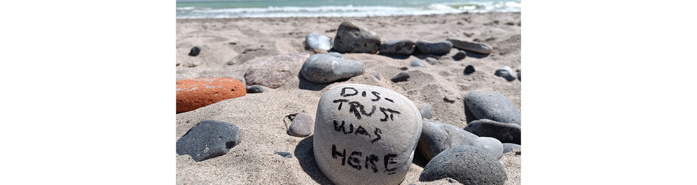DIS-TRUST written on a stone on the beach