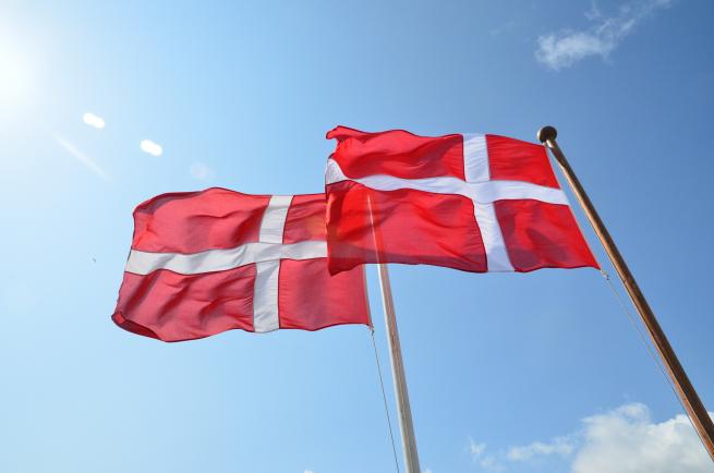 2 danske flag på flagstang blæser i vinden en sommerdag med blå himmel