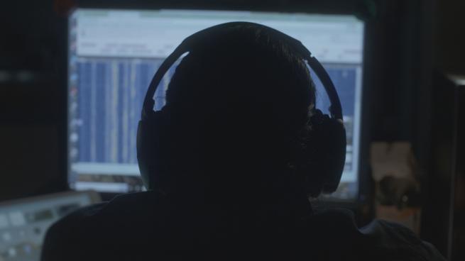 Person with headphones looking at computer screen in a dark room