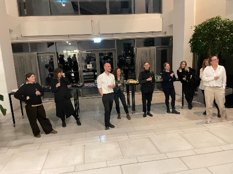 Nine people standing in a lobby, facing slightly rightwards, smiling and listening to a speech addressed for one of them, a PhD candidate in the center of the group in the photo, two steps in front.