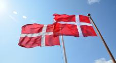 2 danske flag på flagstang blæser i vinden en sommerdag med blå himmel